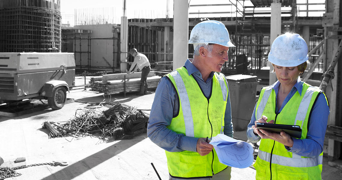 A man and a woman wearing personal protective equipment talk on a construction site