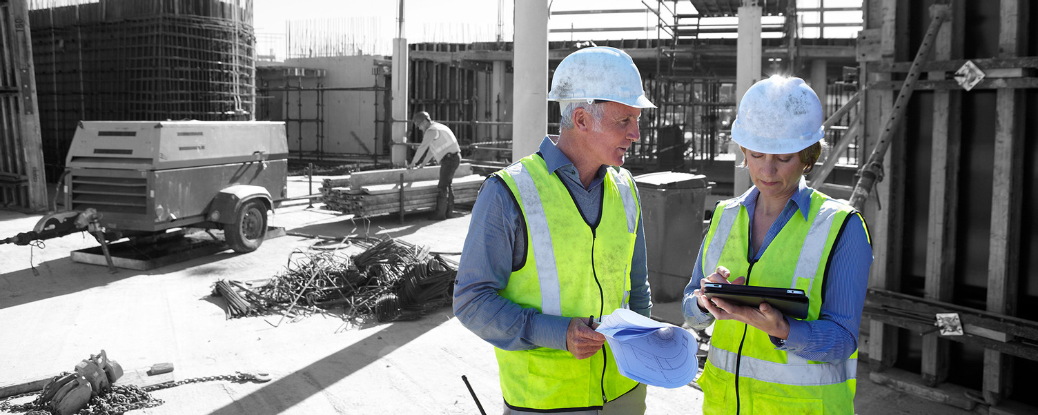 Project team of a man and a woman with hard hat and high visual vest at a construction site