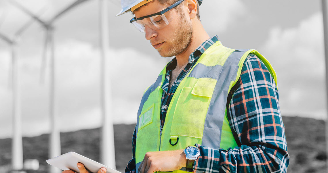 A foreman wearing personal protective equipment uses an iPad at a wind farm